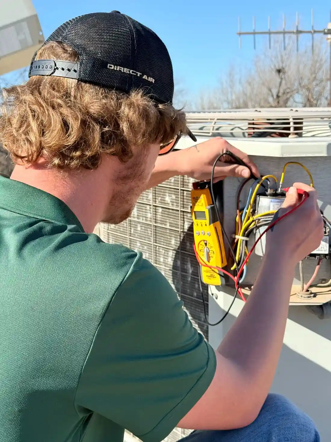 Technician checking electrical connections on outdoor equipment with yellow meter