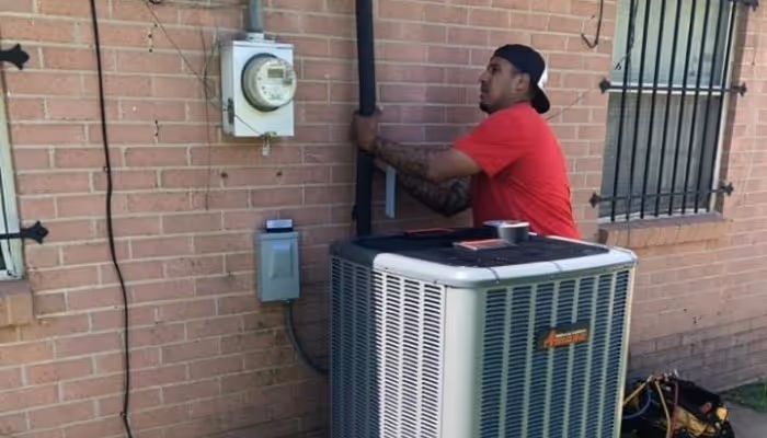 Technician in red shirt repairing air conditioning unit on brick wall