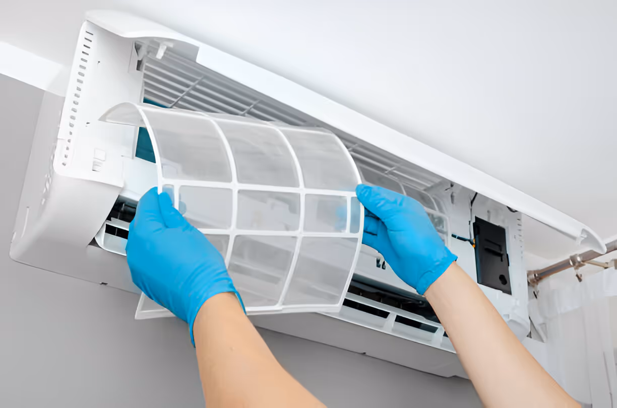 Hands in blue gloves removing air filter from white air conditioning unit