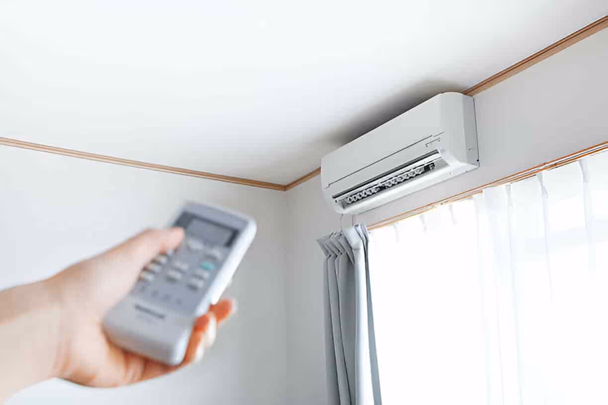 Hand holding remote control pointed at wall-mounted air conditioner