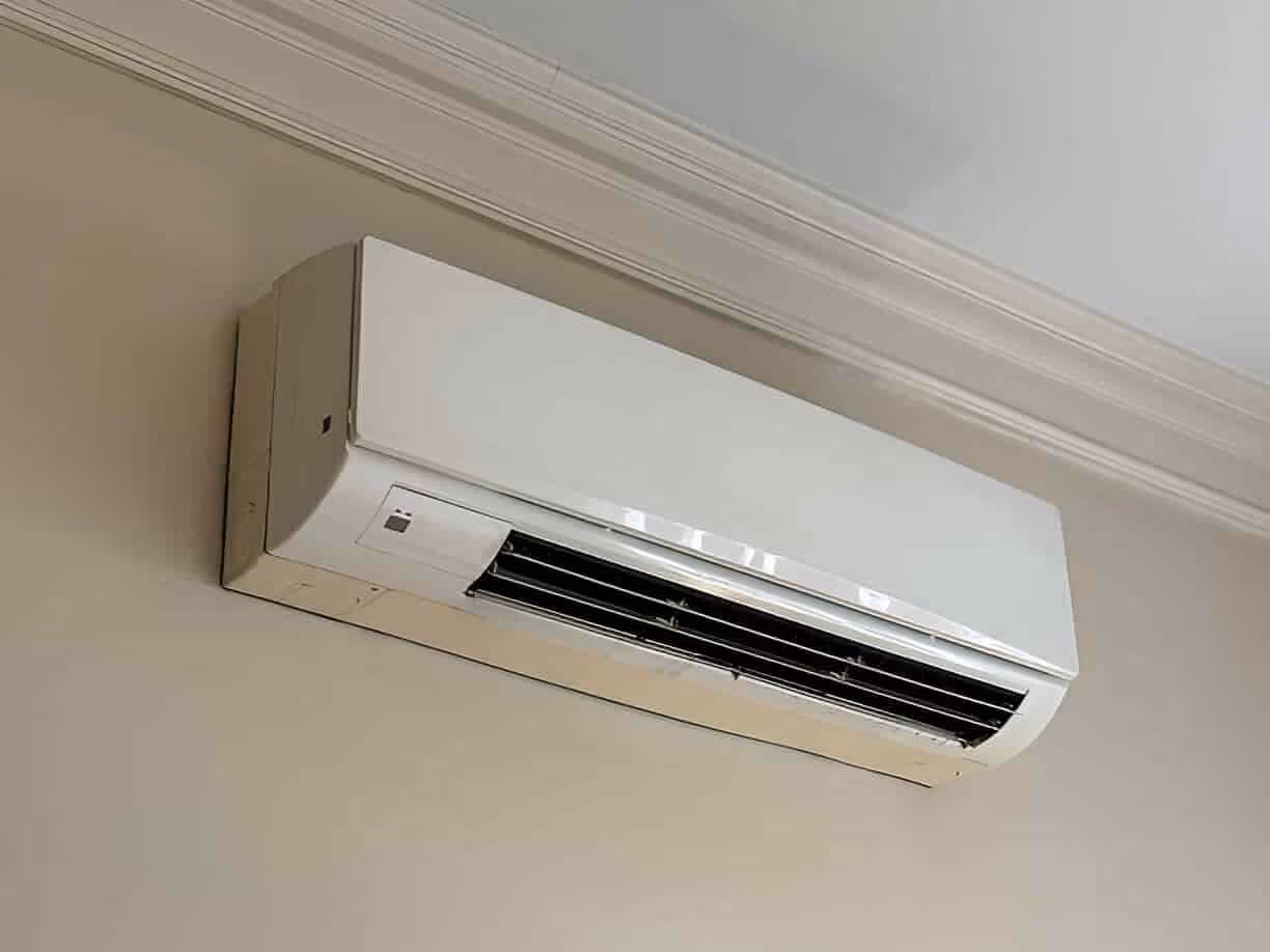 White wall-mounted air conditioning unit with vents against beige wall