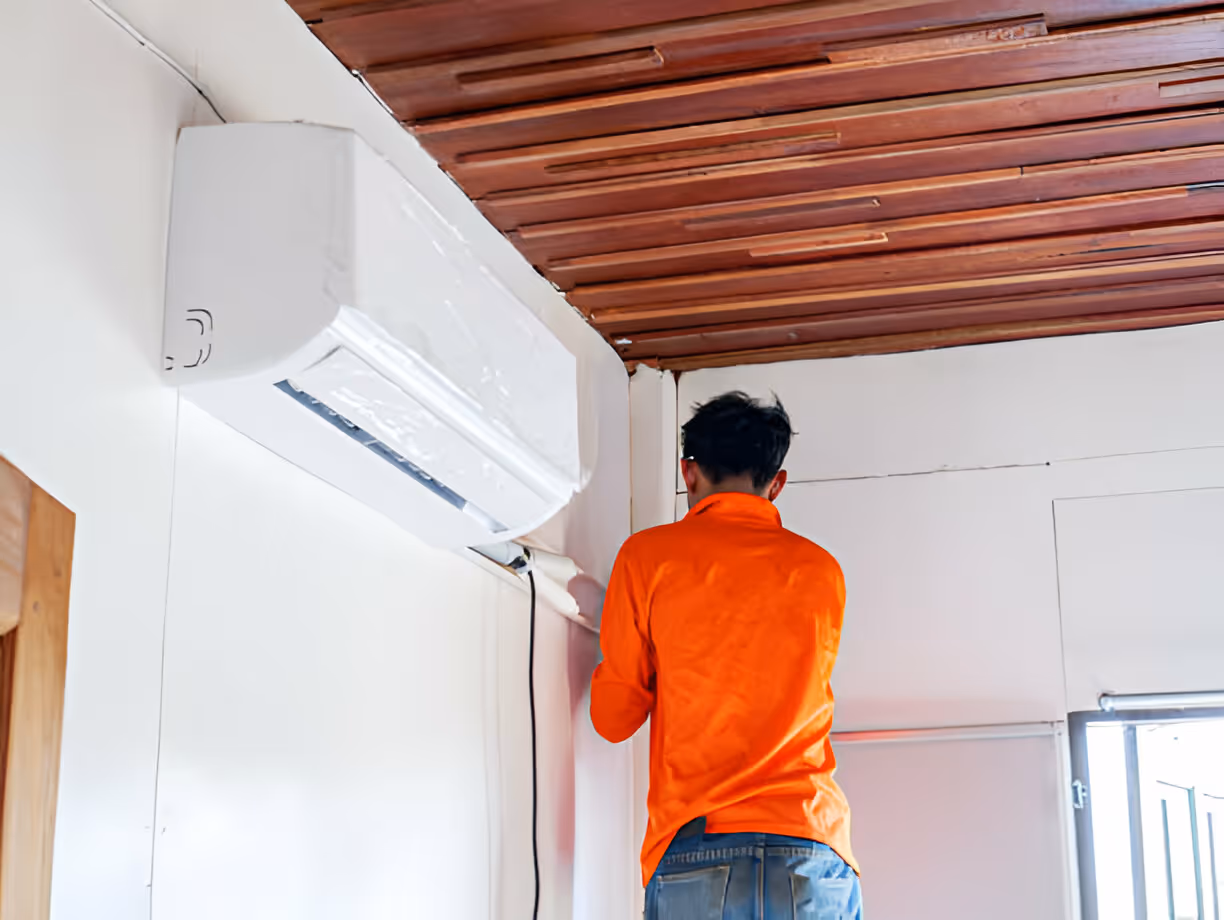 Technician in orange shirt installing or checking wall-mounted air conditioner