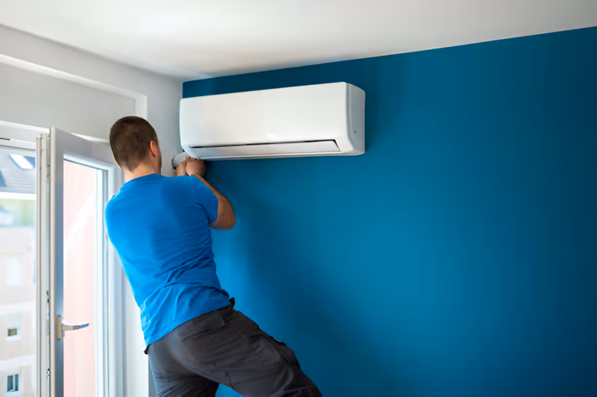 Technician installing a white air conditioning unit on a blue wall