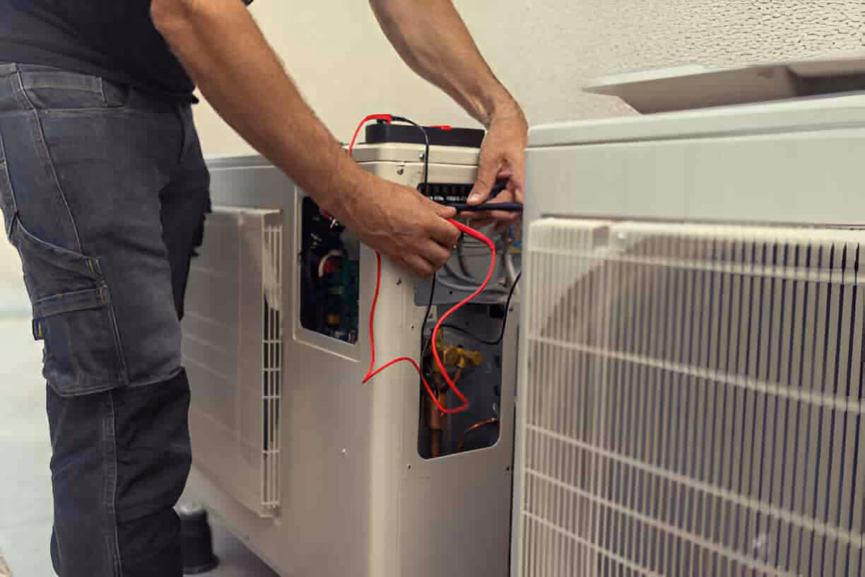 Technician repairing air conditioning unit with red electrical wires