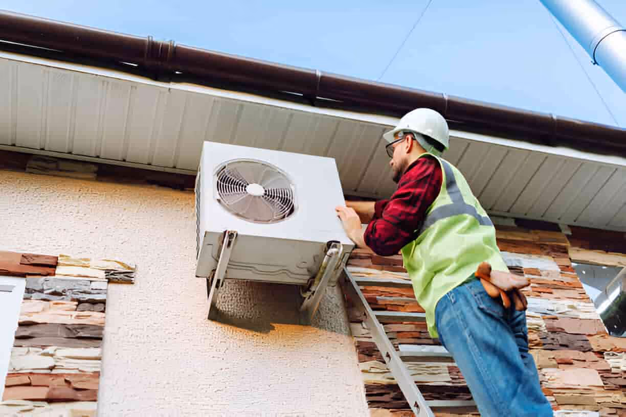 Worker in safety vest checks outdoor air conditioning unit on building