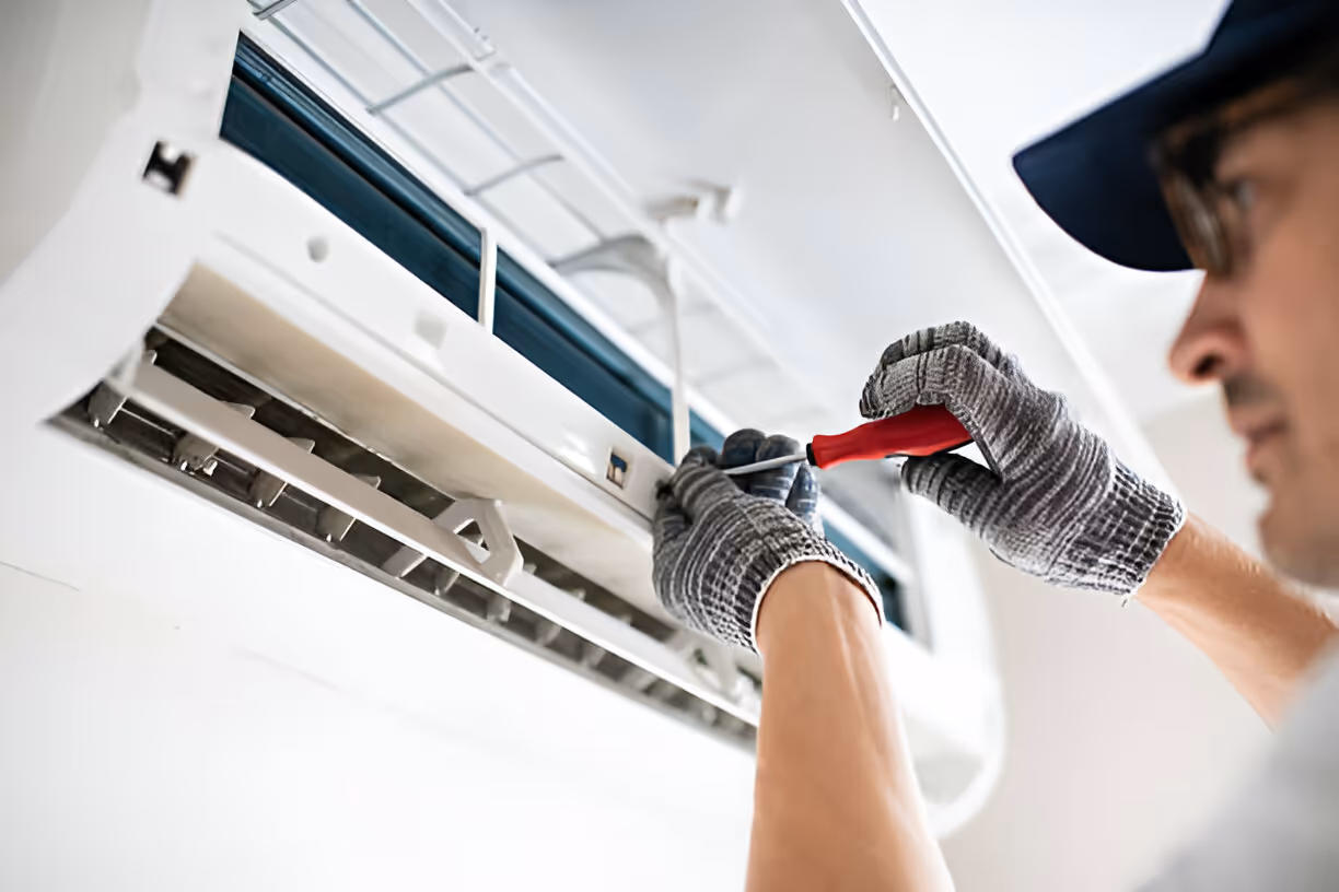 Technician repairing air conditioning unit with screwdriver