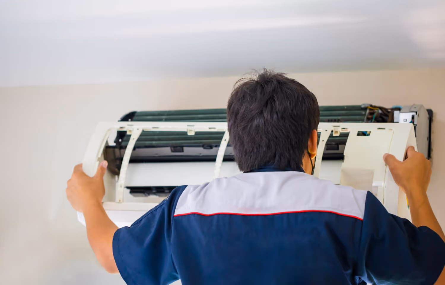 Technician installing air conditioning unit on white wall