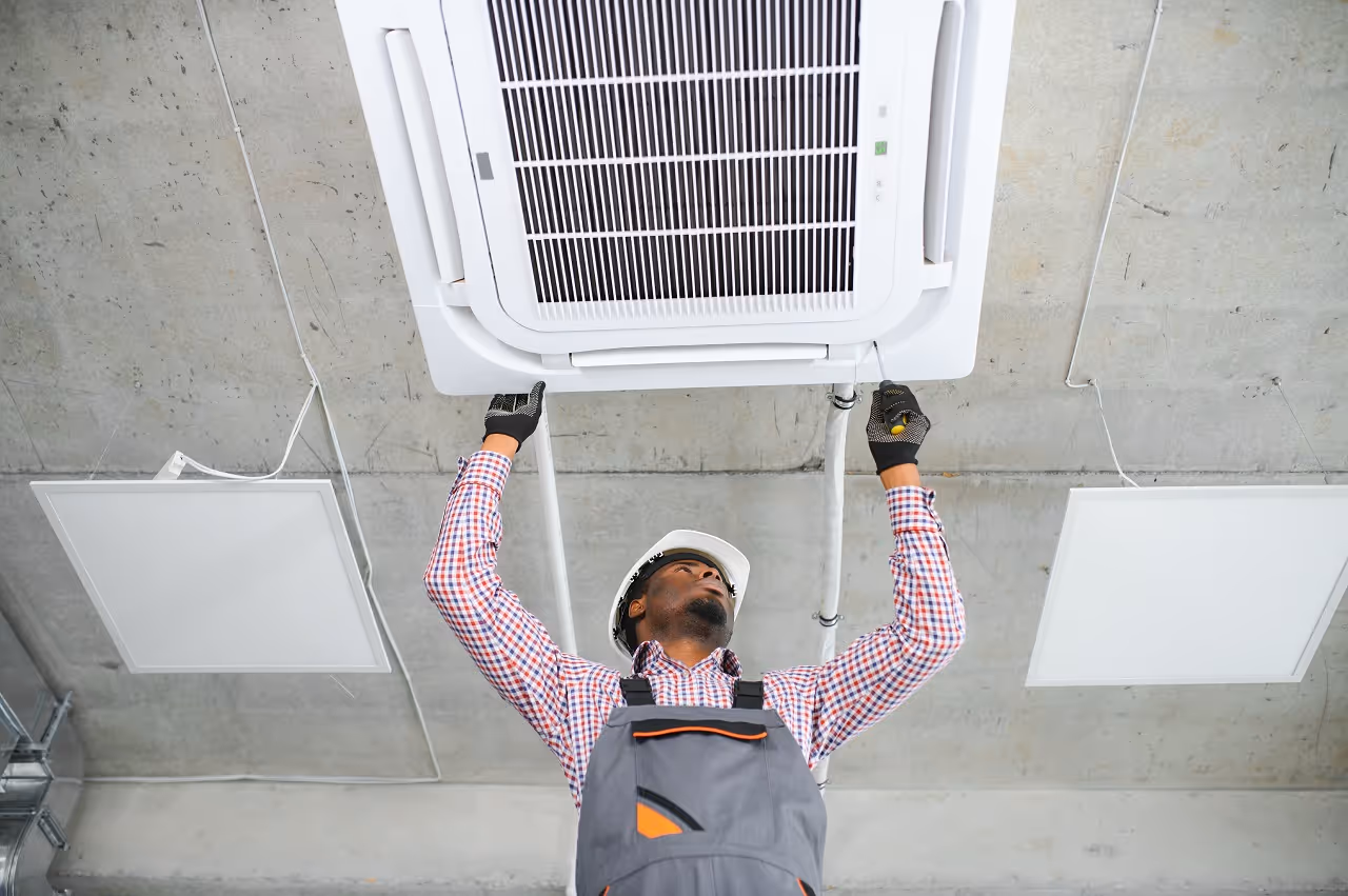 Technician in hard hat installing ceiling air conditioning unit