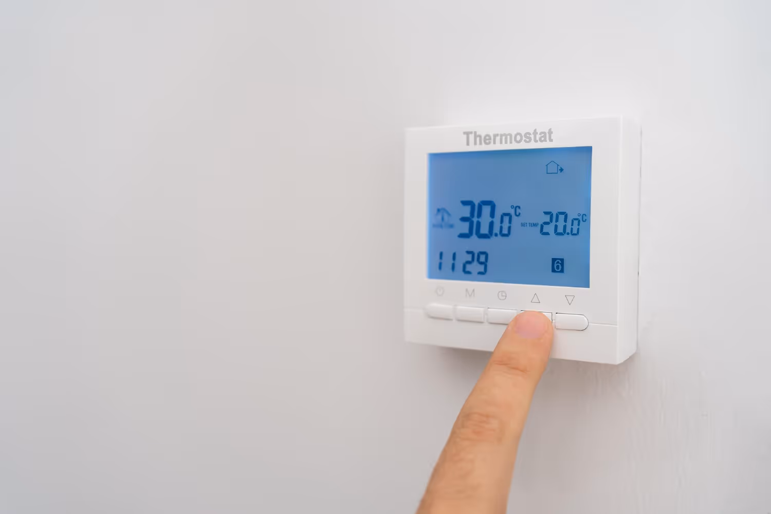 Hand adjusting digital thermostat showing 30°C and 20.6°C temperatures