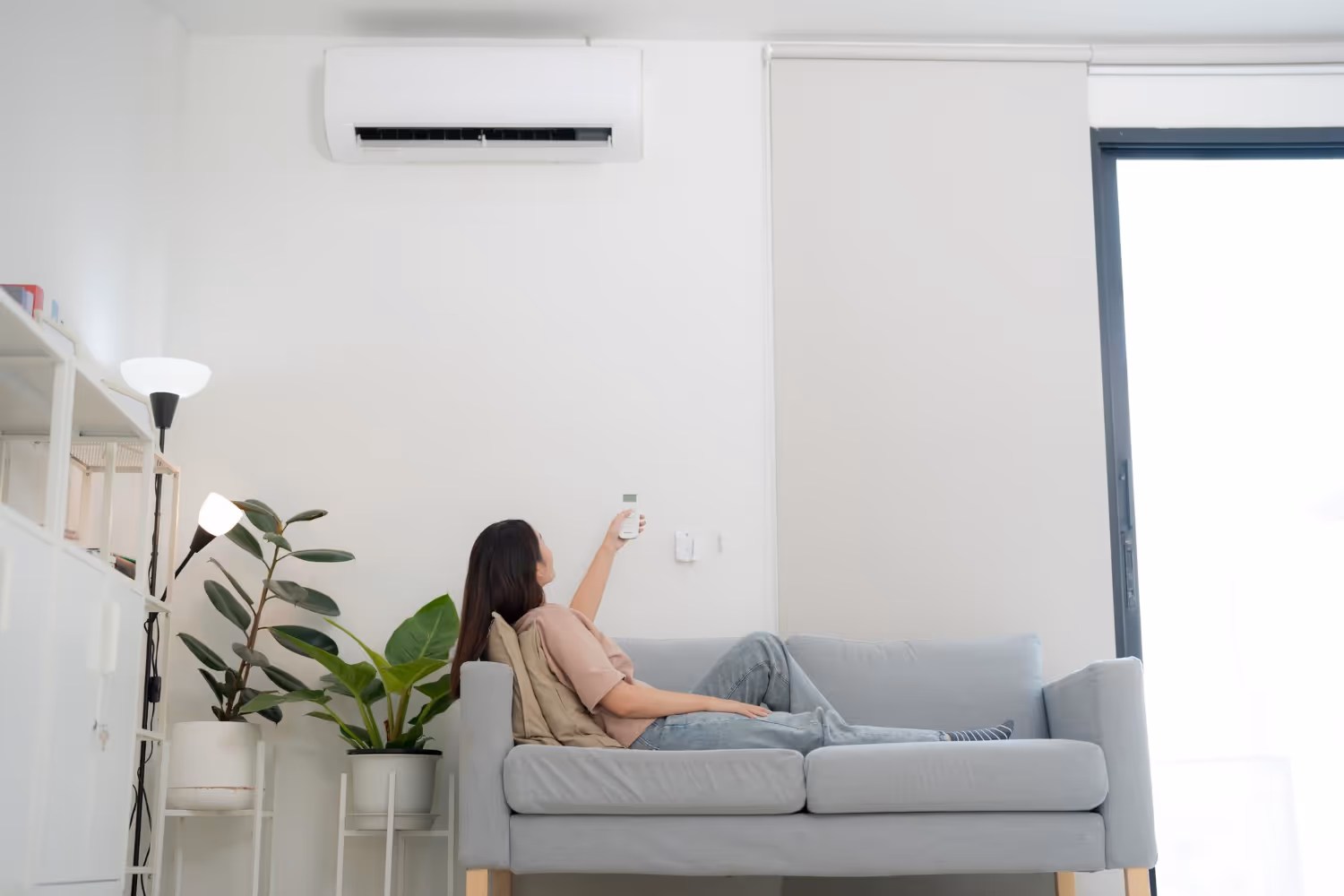 Person relaxing on gray couch adjusting air conditioner at home
