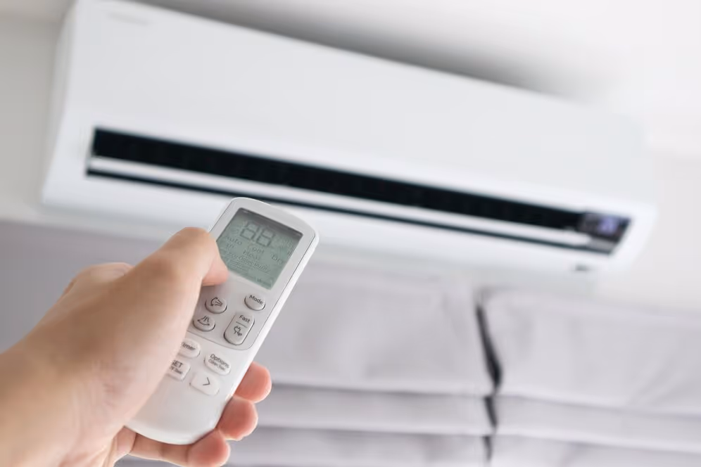 Hand holding air conditioner remote control with unit mounted on wall