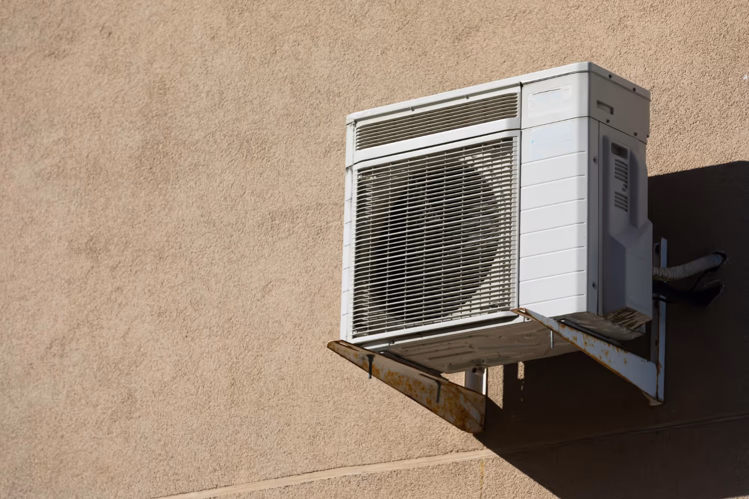 Old air conditioning unit mounted on rusty bracket against textured wall