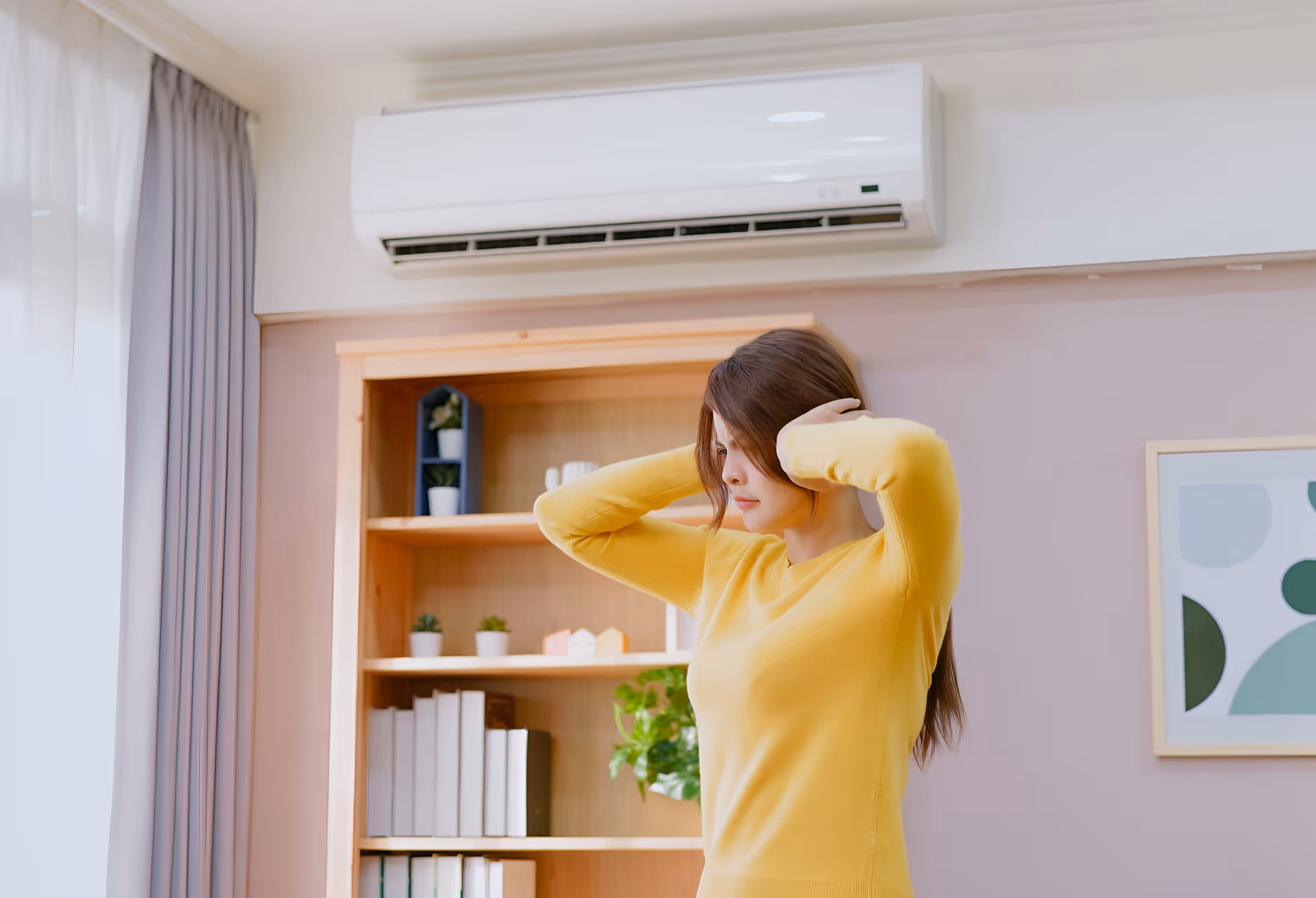 Person in yellow sweater stretching near bookshelf with air conditioner