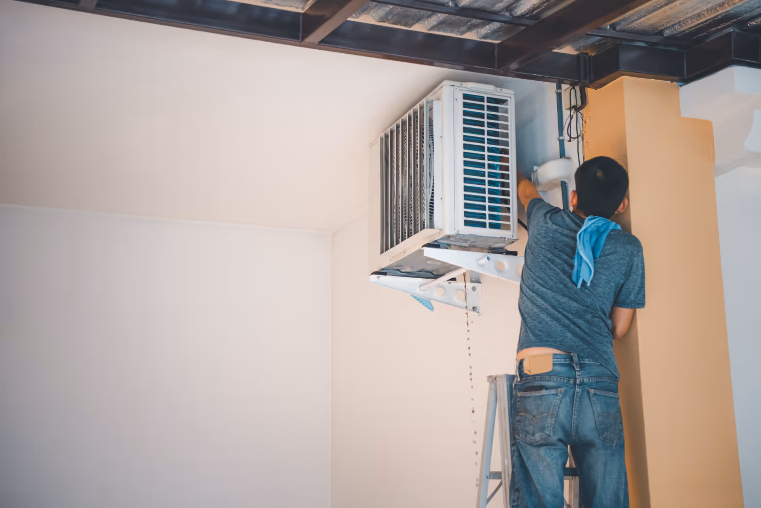 Technician on ladder repairing air conditioning unit against white wall