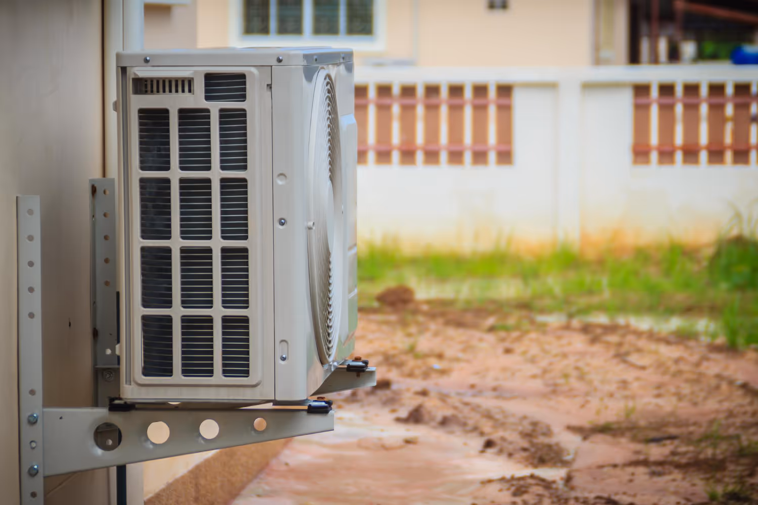 White air conditioning unit mounted on exterior wall near grassy backyard