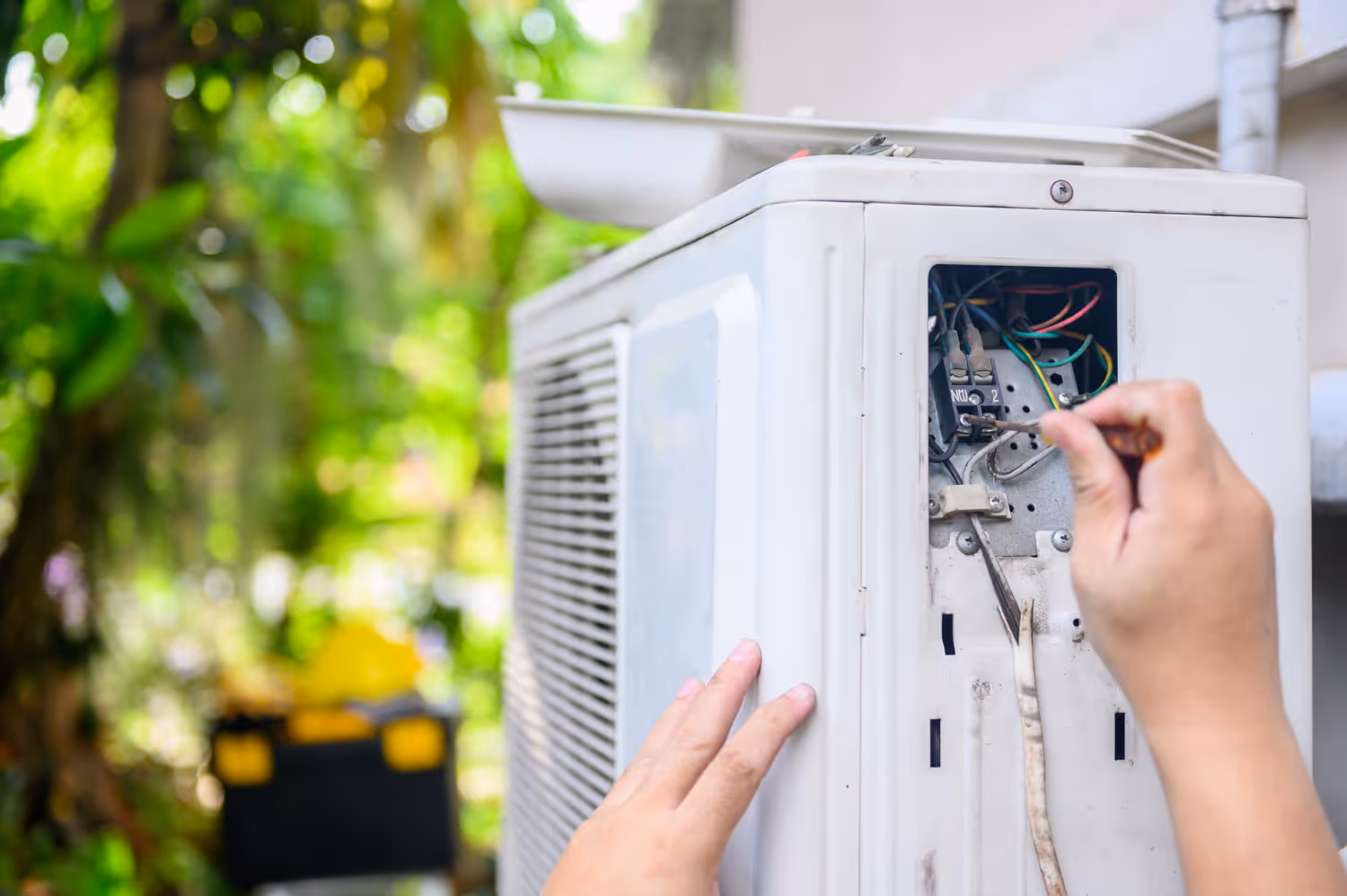 Technician repairing air conditioning unit with screwdriver outdoors