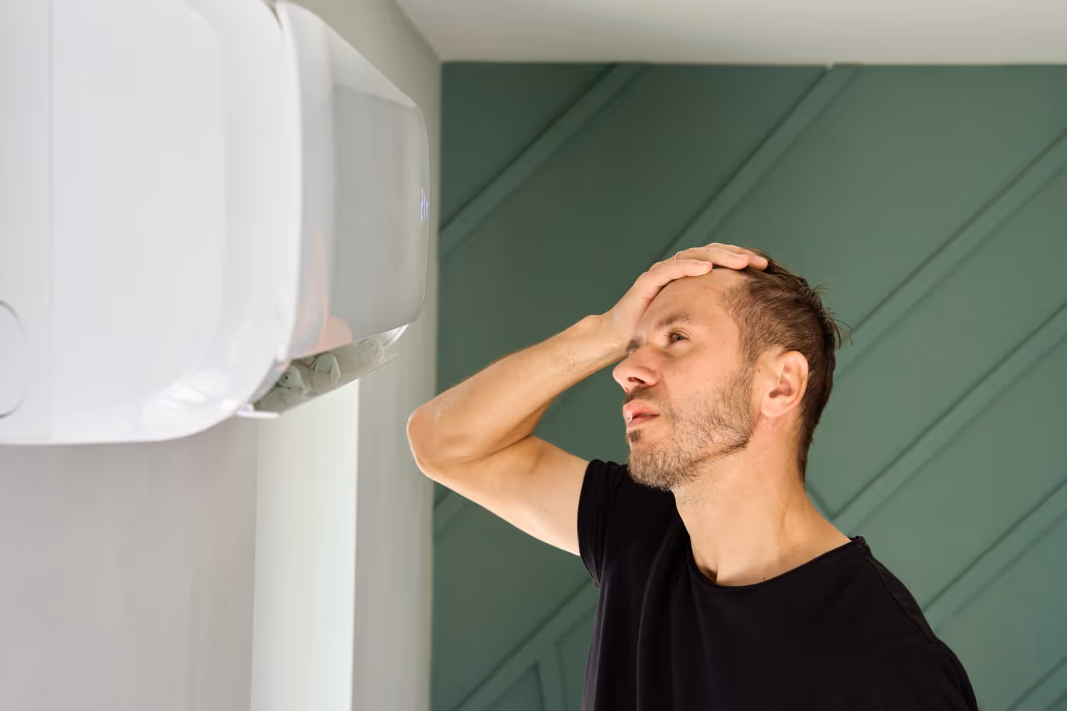 Person looking stressed near a white thermostat on green wall