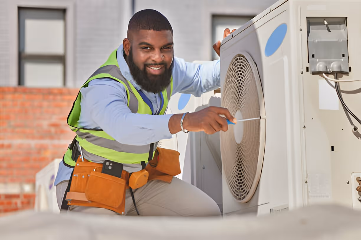 Technician in safety vest repairing air conditioning unit outdoors