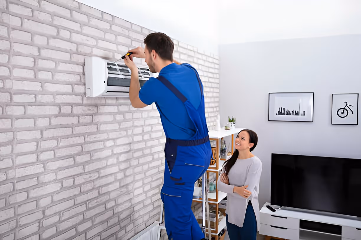 Technician in blue uniform installing air conditioning unit in living room