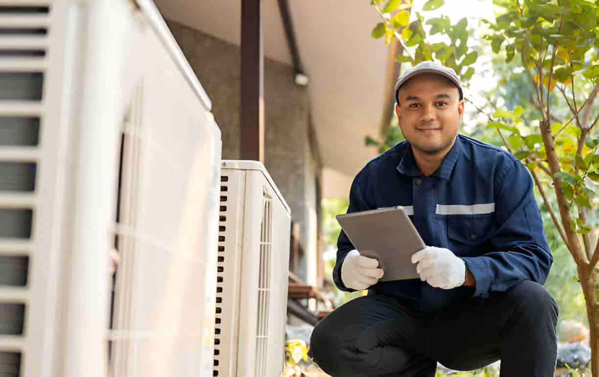 Technician in blue uniform checking air conditioning unit with tablet