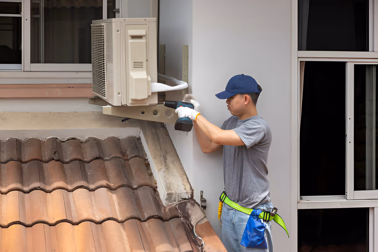 Technician installing air conditioning unit on exterior wall