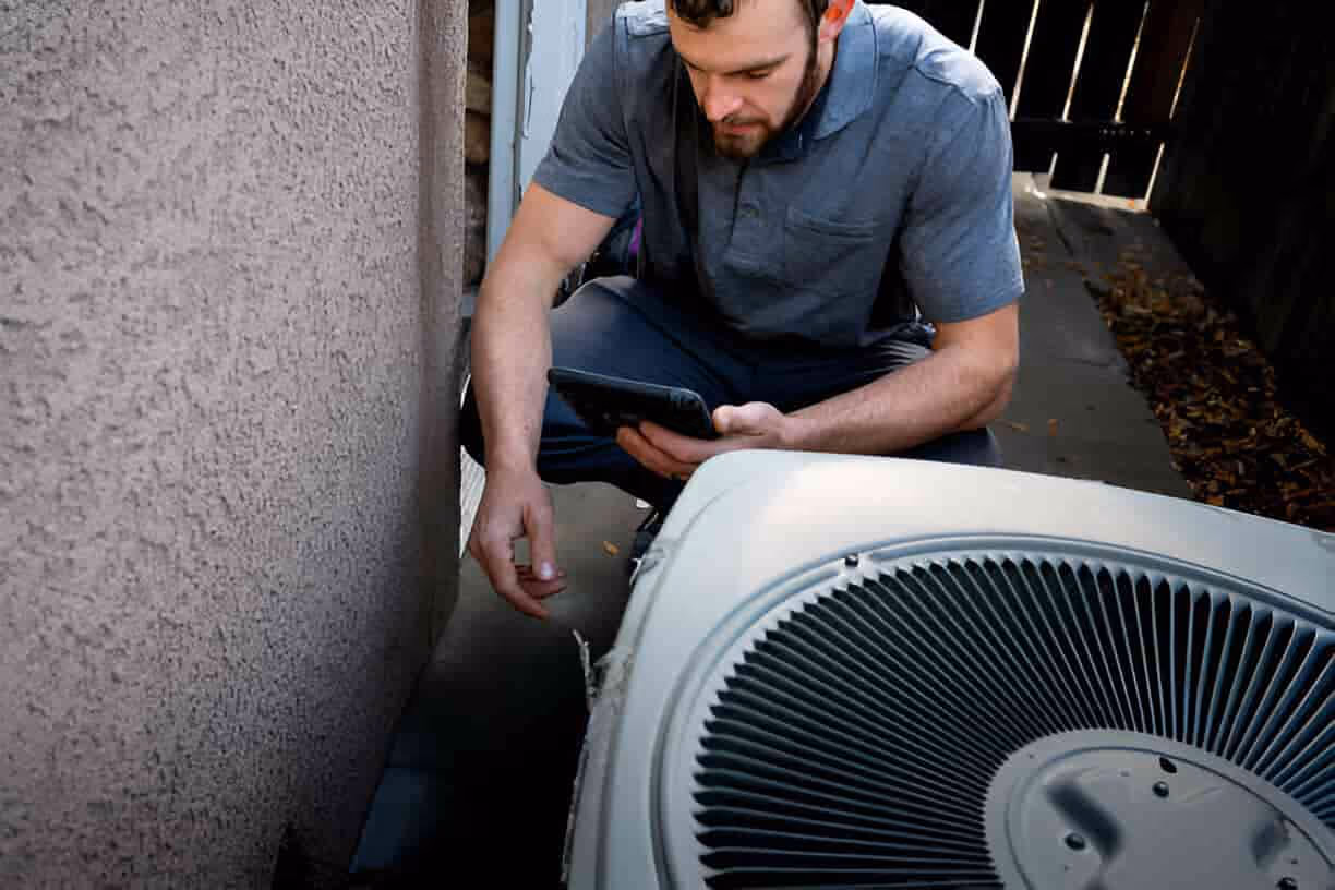 Technician checking HVAC unit using tablet near outdoor air conditioning system