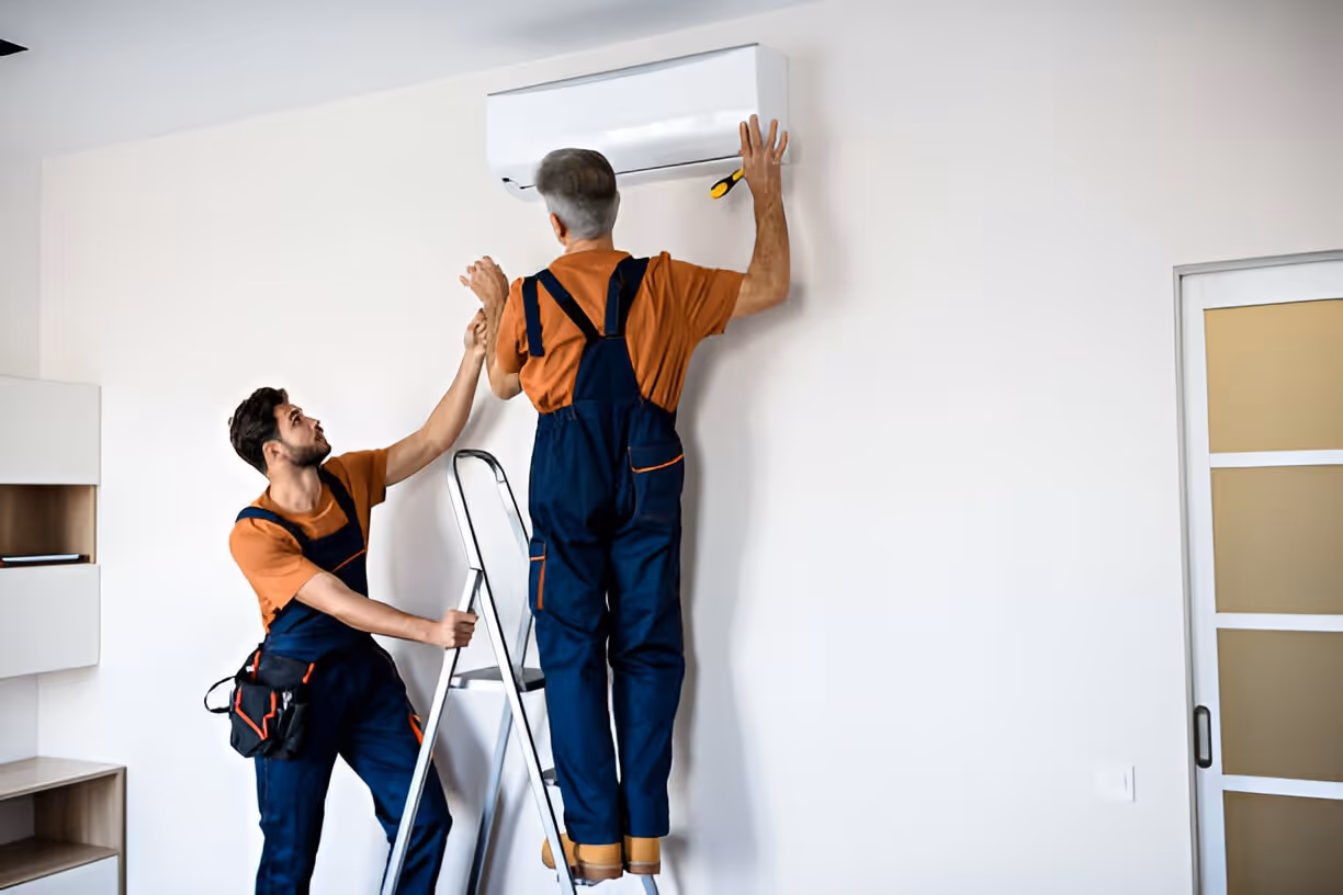 Two workers installing air conditioning unit on white wall
