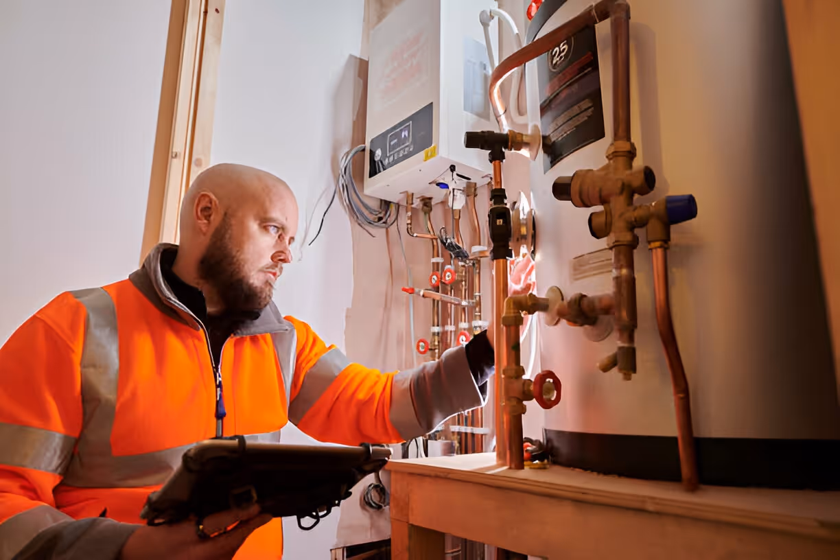 Technician in orange vest checking industrial piping and electrical system