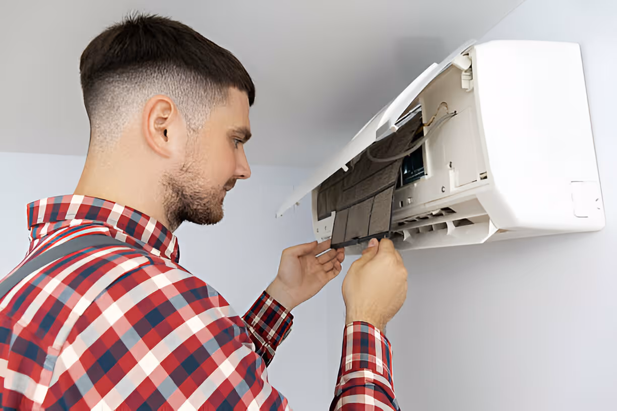 Technician in plaid shirt repairing wall-mounted air conditioning unit
