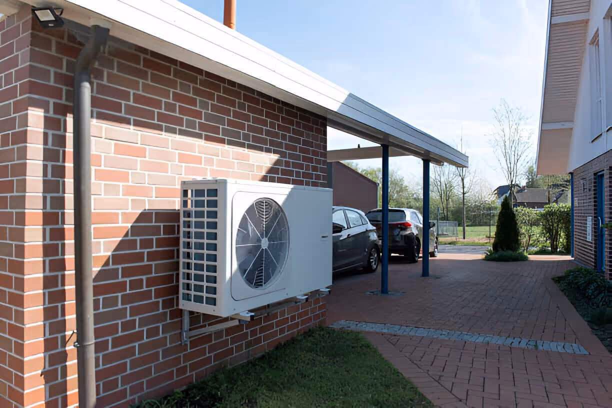 Heat pump unit mounted on brick wall with carport and parked cars