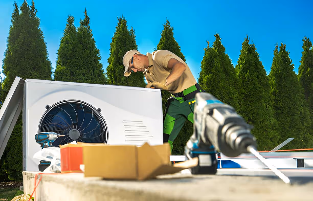HVAC technician installing air conditioning unit near green trees