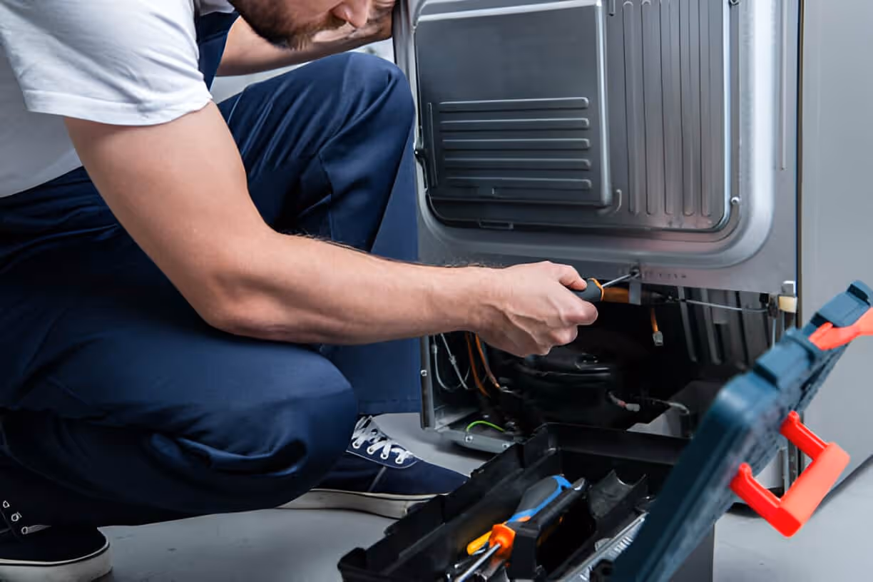 Technician repairing appliance, working on internal components with tools