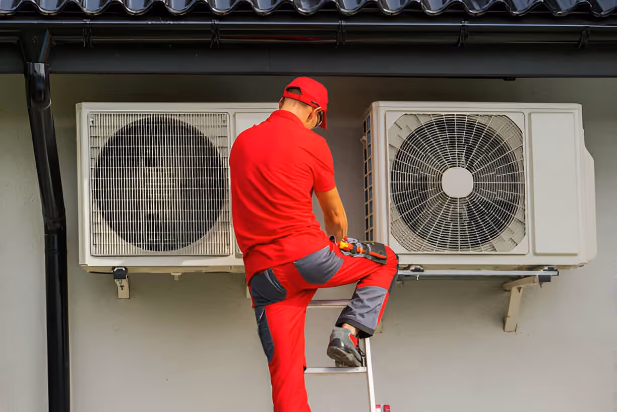 Technician in red uniform servicing air conditioning units on wall