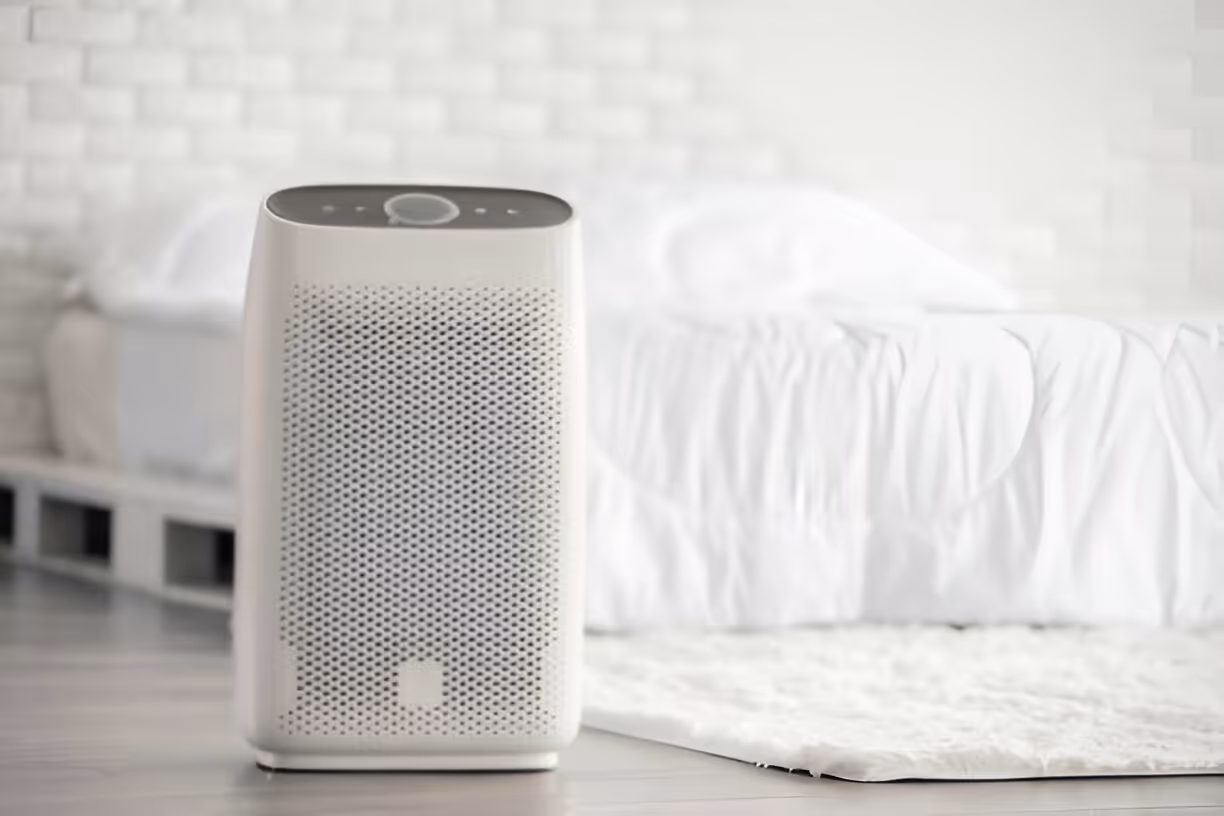 White air purifier on floor next to bed in minimalist bedroom