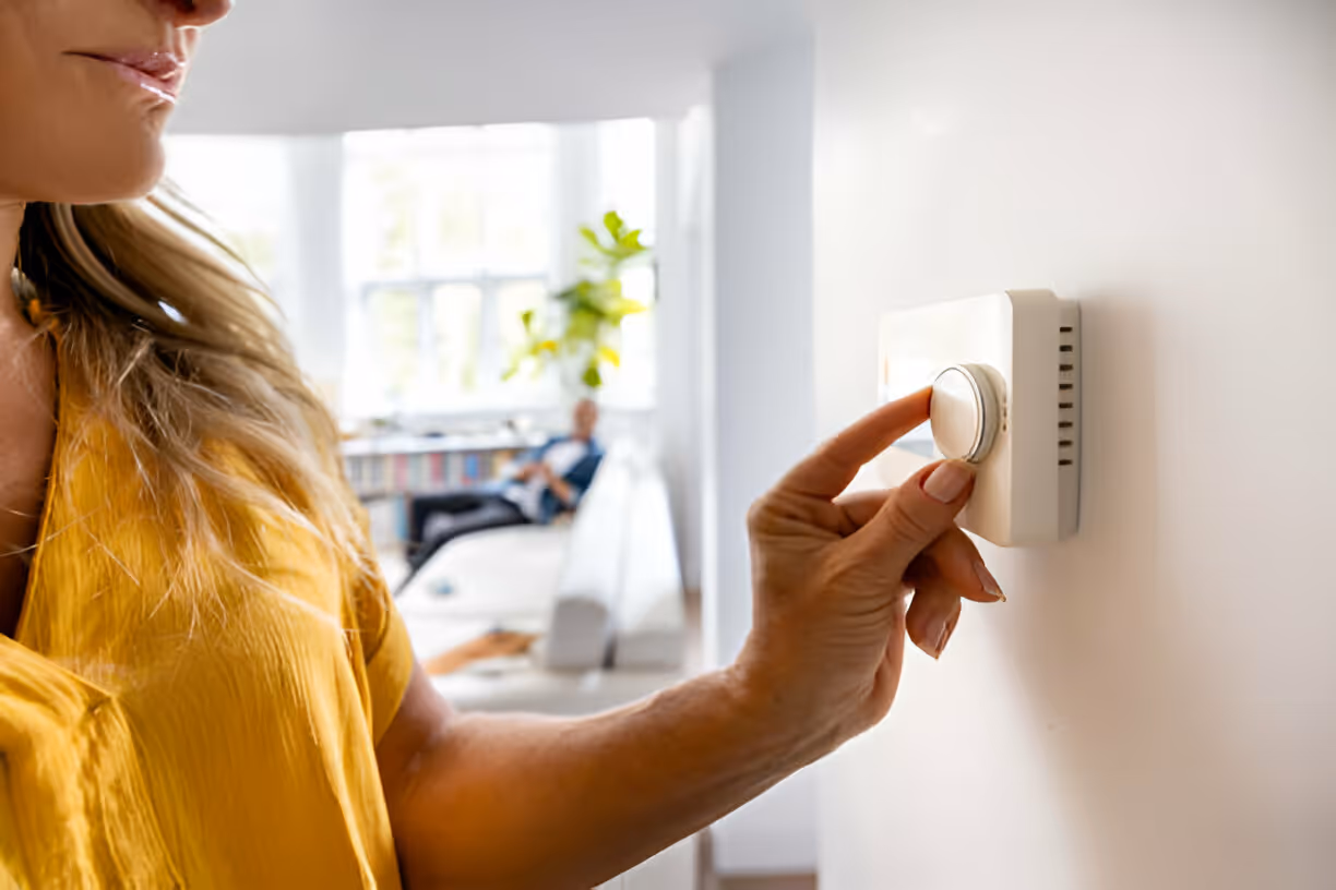 Person in yellow shirt adjusting smart home thermostat near window