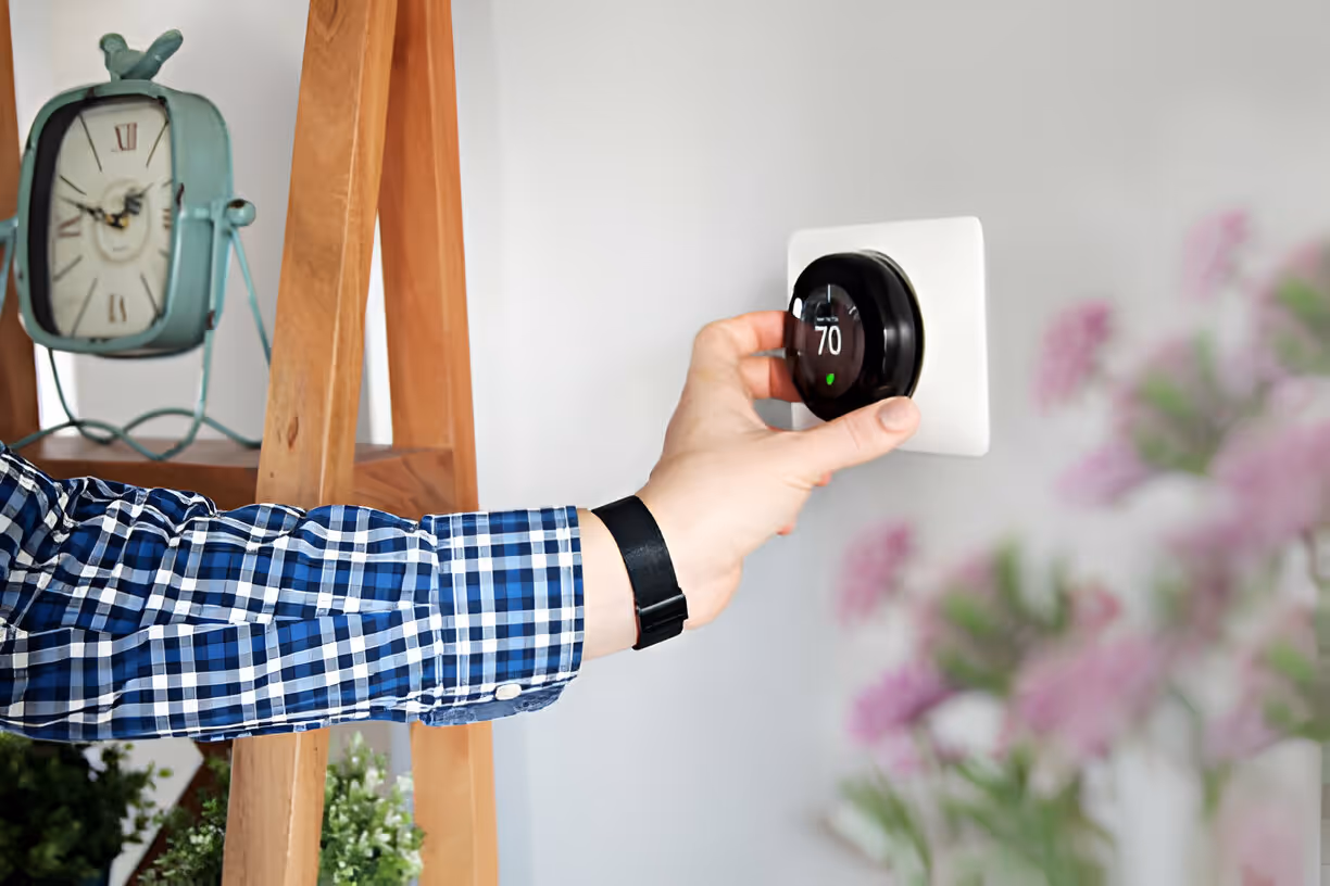 Hand adjusting smart thermostat next to vintage clock and blurred flowers