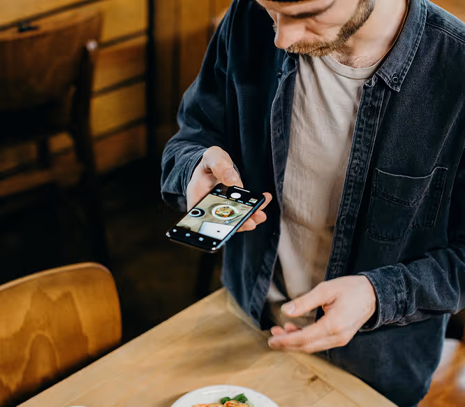 Content creator taking a photo of food with a smartphone, capturing aesthetic visuals for Instagram using Kicksti’s engagement tools.