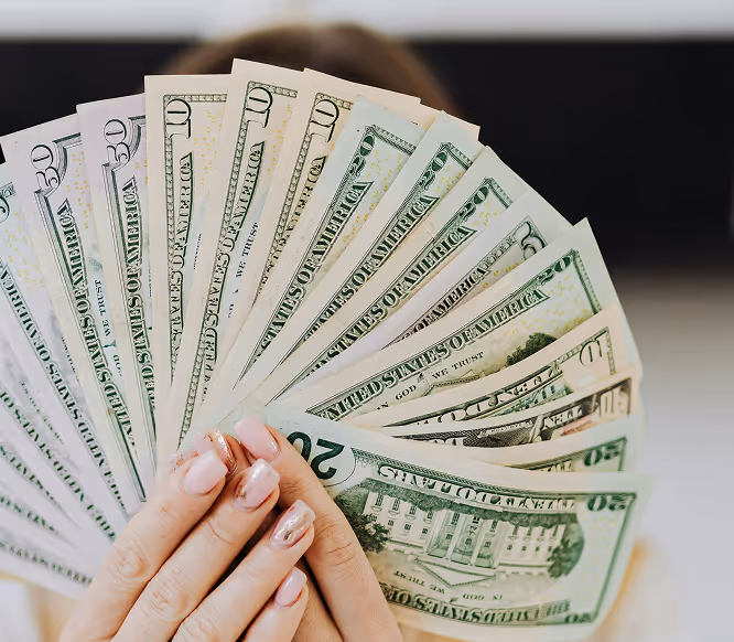 Hands holding a fan of US dollar bills, symbolizing revenue growth and monetization potential through Instagram marketing with Kicksti.