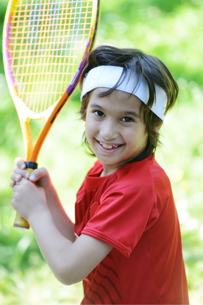 Smiling young child holding a tennis racket, illustrating early dental care for happy, healthy smiles.