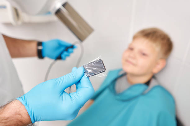 Doctor pointing X-ray unit holding electronic sensor in child. Dentist prepares boy for tooth x-ray image in dental clinic. Radiographer taking teeth radiography to a boy using digital x-ray machine in pediatric dental clinic. Dentist prepares boy for tooth x-ray image in dental clinic Close-up of a child smiling in a dental chair while a clinician gently positions a small digital sensor stock pictures, royalty-free photos & images