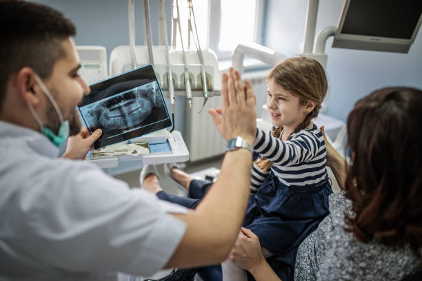 A child with a dentist in a dental office A child with a dentist in a dental office Dentist kneeling to eye level with a child, both smiling; monitor in the background with a blurred dental x-ray stock pictures, royalty-free photos & images