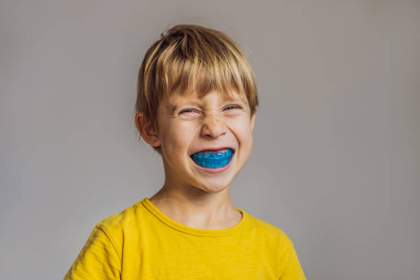 Six-year old boy shows myofunctional trainer. Helps equalize the growing teeth and correct bite, develop mouth breathing habit. Corrects the position of the tongue Six-year old boy shows myofunctional trainer. Helps equalize the growing teeth and correct bite, develop mouth breathing habit. Corrects the position of the tongue. 9-year-old Child at a follow-up exam smiling with a custom mouthguard case; bright clinic, happy mood] stock pictures, royalty-free photos & images