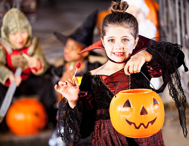 Little girl in halloween costume Little girl (6 years) wearing halloween costume, with candy apple. female Child in vampire costume holding a pumpkin candy bucket, smiling  stock pictures, royalty-free photos & images