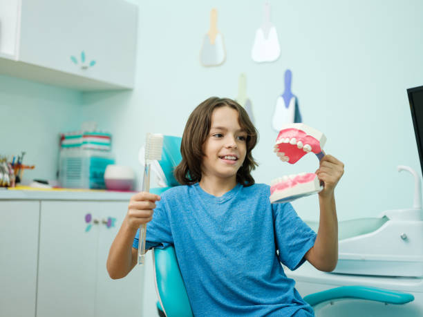 Latin boy holding big toothbrush and model teeth in dental office
