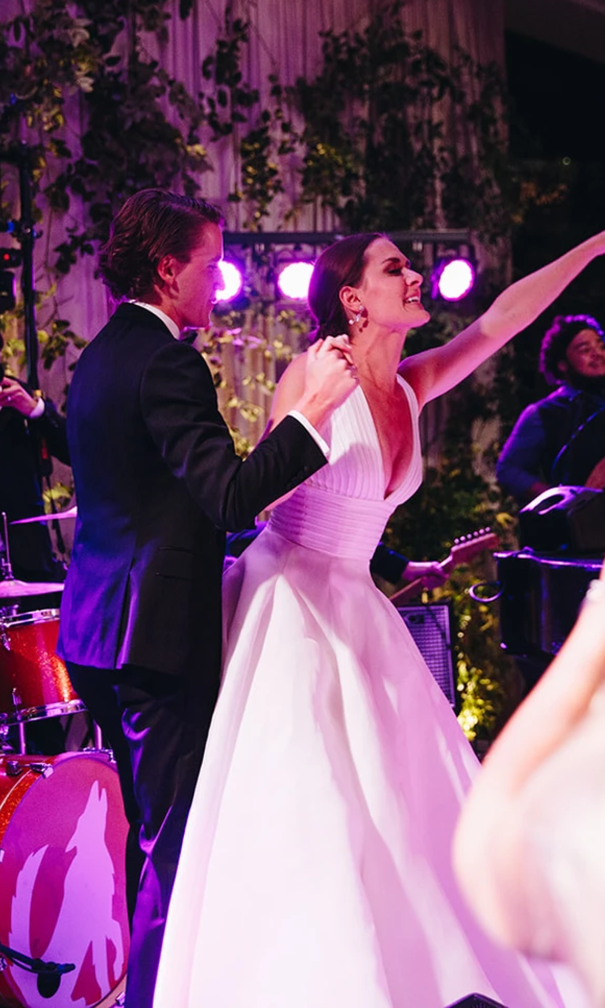Image of a bride and groom, surround by musicians and guests under pink and purple lighting