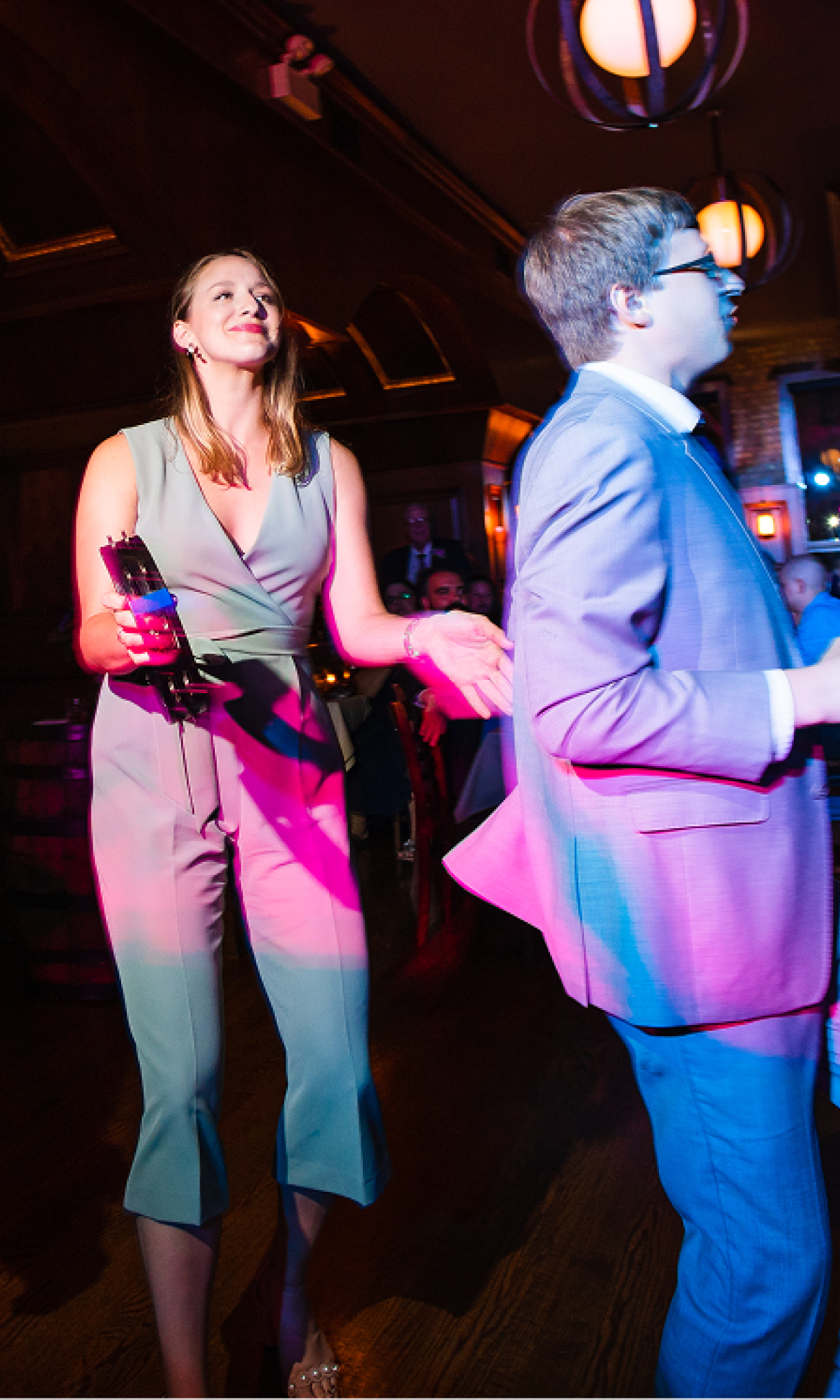 Five people in business casual attire at a music venue, with a crowd of guests in the background; one person is playing a tambourine.