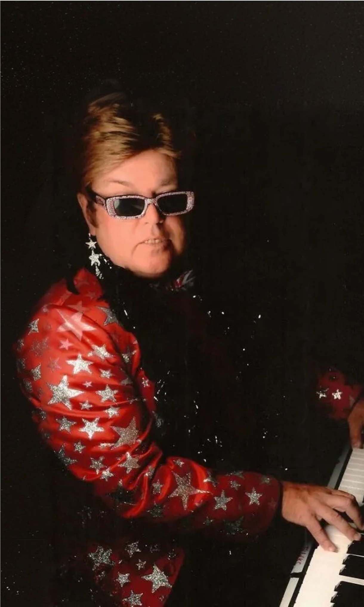 Man in red suit and sunglasses playing a piano