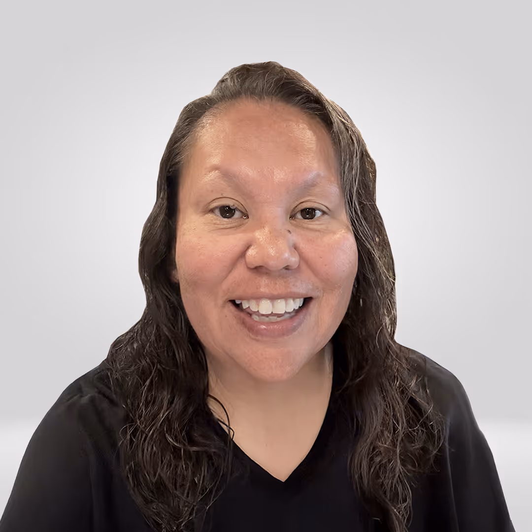 Smiling woman with long wavy dark hair wearing a black shirt against a plain gray background.