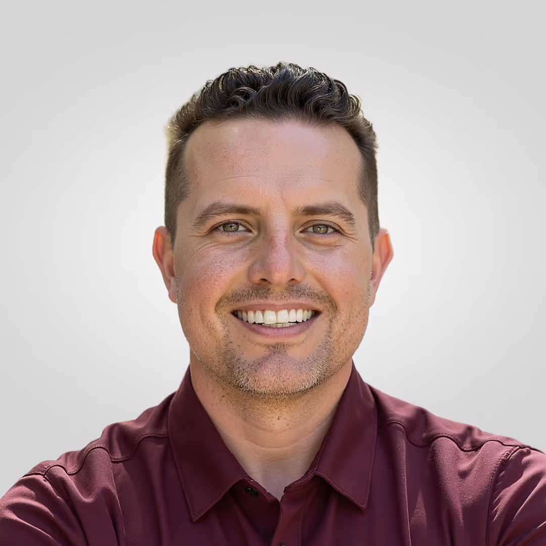 Smiling man with short curly hair wearing a maroon shirt against a plain light gray background.
