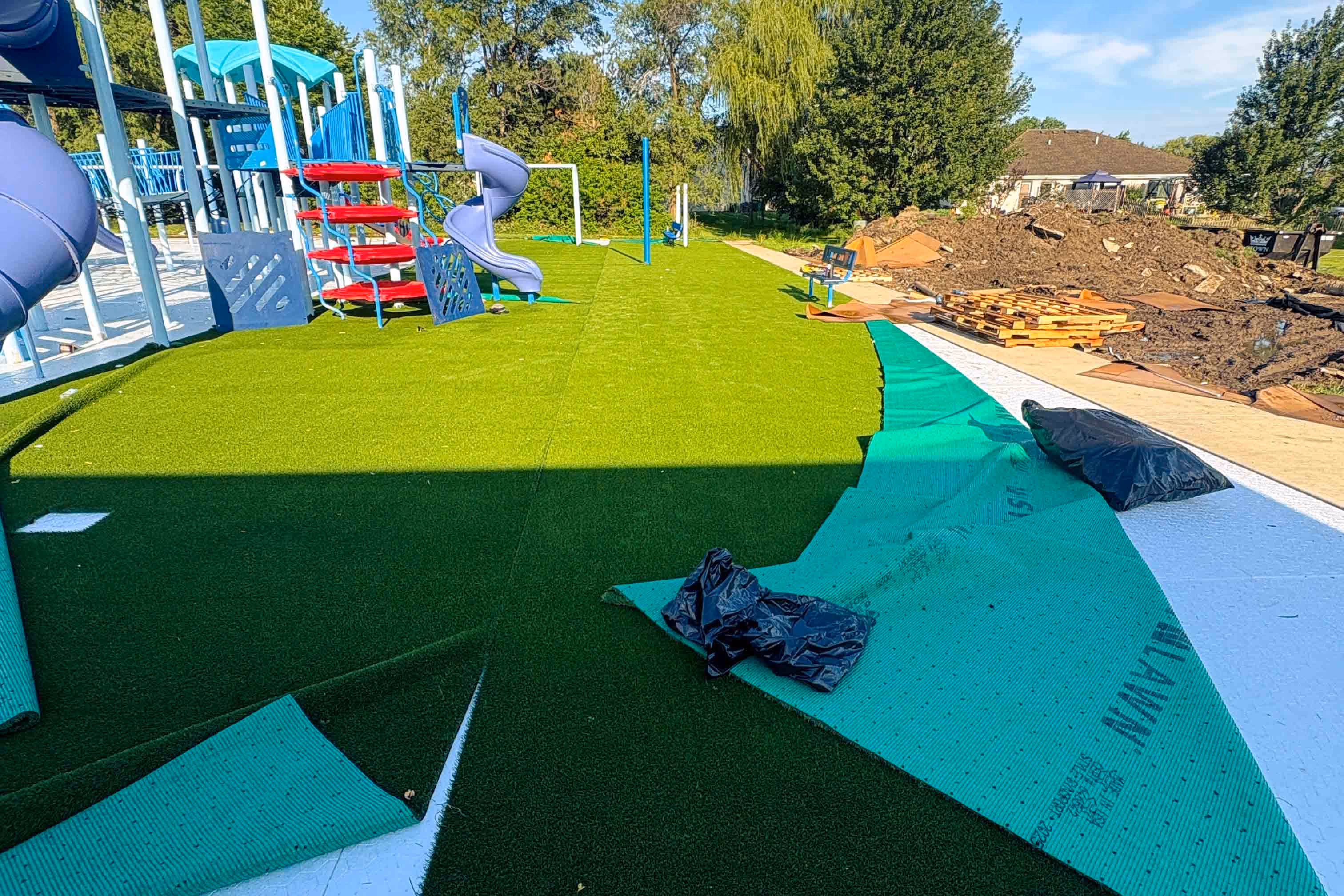 Playground under construction with slides and turf being installed on ground.